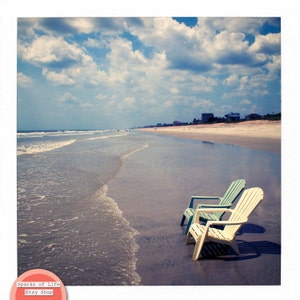 Peut inclure: Deux chaises de plage sur une plage de sable avec de l'eau bleue et un ciel nuageux. Les chaises sont tourn&eacute;es vers l'oc&eacute;an. Une chaise est bleu clair et l'autre est blanche.