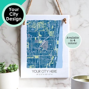 May include: A white canvas print with a blue and green map of a city. The map is titled "YOUR CITY HERE" and includes the coordinates "26 22 27 N/80° 4' 5T W". The text "Available in 4 colors!" is in a circle in the bottom right corner.