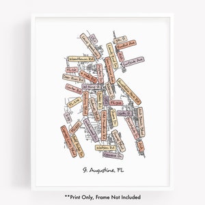 May include: A hand-drawn map of St. Augustine, Florida, with street names and landmarks highlighted in various shades of pink, orange, and brown. The map is framed in a white frame with the text "Print Only, Frame Not Included" below the map.