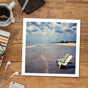 Peut inclure: Une photographie encadr&eacute;e d'une sc&egrave;ne de plage avec deux chaises de plage bleues et blanches sur le sable. Les chaises font face &agrave; l'oc&eacute;an, qui est d'un bleu clair avec des vagues blanches. Le ciel est d'un bleu clair avec des nuages blancs.