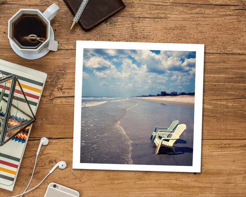 Peut inclure: Une photographie encadr&eacute;e d'une sc&egrave;ne de plage avec deux chaises de plage bleues et blanches sur le sable. Les chaises font face &agrave; l'oc&eacute;an, qui est d'un bleu clair avec des vagues blanches. Le ciel est d'un bleu clair avec des nuages blancs.