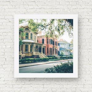 May include: A row of colorful historic houses with white trim and green foliage in front. The houses have a variety of architectural styles, including Victorian and Colonial. The houses are located on a street with a paved road and sidewalks.