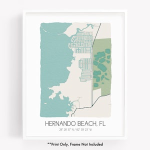 May include: A framed map print of Hernando Beach, FL, featuring a teal and beige color scheme. The map includes the town's name and coordinates. The print is displayed in a white frame.