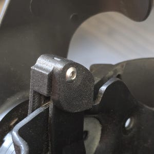 May include: Close-up of a black plastic part with a small silver screw. The part has a textured surface and appears to be a component of a larger device.