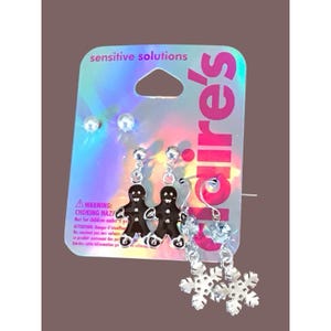 May include: A selection of earrings on a Claire's branded card. The earrings feature silver studs, gingerbread man dangles, blue heart dangles, and snowflake dangles. The card has the text "sensitive solutions" and a choking hazard warning.