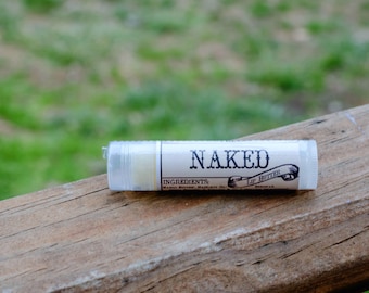 Puede incluir: Un tubo blanco de bálsamo labial con una etiqueta negra que dice "NAKED Lip Butter". La etiqueta también incluye el texto "INGREDIENTS: Mango Butter,  Shea Butter,  Hazelnut Oil".