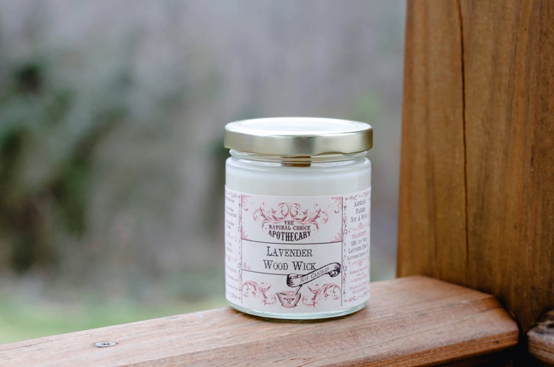 Puede incluir: Un tarro de vela blanco con tapa dorada y una etiqueta que dice "The Natural Choice Apothecary Lavender Wood Wick".