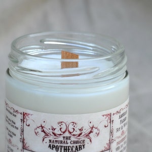 Puede incluir: Una vela blanca en un tarro de vidrio transparente con una mecha de madera. El tarro tiene una etiqueta que dice "The Natural Choice Apothecary".