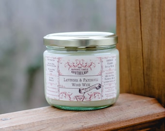 Puede incluir: Una vela de vidrio en un frasco con tapa dorada y una etiqueta blanca. La etiqueta dice "The Natural Choice Apothecary" y "Lavender & Patchouli Wood Wick".