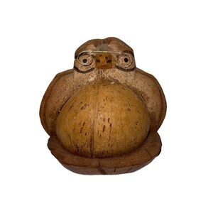 Könnte beinhalten: Handgefertigte Eulenfigur aus einer Kokosnussschale geschnitzt. Die Eule hat einen runden Körper, Flügel und einen Kopf mit kleinen Brillen mit Drahtgestell. Die Augen der Eule sind schwarz bemalt, und der Schnabel ist ein kleines, rechteckiges Holzstück.