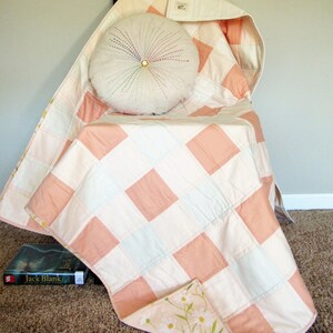 May include: A pink and white patchwork quilt with a floral print on the back. The quilt is folded and draped over a chair with a white round pillow on top.