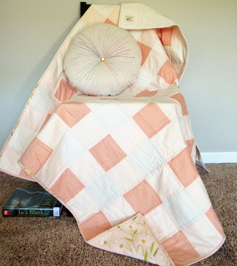 May include: A pink and white patchwork quilt with a floral print on the back. The quilt is folded and draped over a chair with a white round pillow on top.