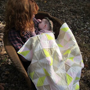 Puede incluir: Una mujer y un bebé están sentados en una silla de mimbre. El bebé está envuelto en una colcha rosa y amarilla. La mujer lleva una camisa a cuadros.