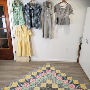 May include: Five vintage dresses hanging on hangers against a white wall. The dresses are in various patterns and colors, including floral, striped, and checkered. The dresses are all in good condition and would be a great addition to any vintage clothing collection.