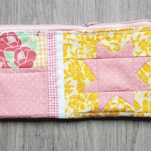 Peut inclure: Une pochette zippée en patchwork rose et jaune avec un motif d'étoile. La pochette est faite de différents tissus avec des motifs floraux et géométriques.