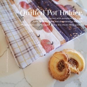 Puede incluir: Un agarrador de cocina acolchado con patrón de cuadros y estampado de calabazas, con el texto Quilted Pot Holder. Seasonally inspired with pumpkins and plaid. 100% hand designed and assembled in PA, USA. Mide 20cm cuadrados con un bolsillo de 15cm.