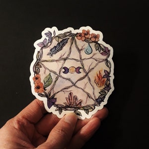 Peut inclure: Un autocollant avec un pentagramme entouré d'éléments floraux et symboliques. Il comprend une plume, une goutte d'eau, du feu et des cristaux, avec un symbole de croissant de lune et de soleil. L'autocollant est sur fond noir.