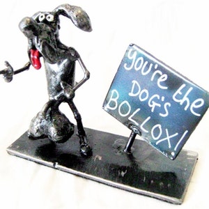 Könnte beinhalten: Eine Metallskulptur eines Hundes, der ein Schild mit der Aufschrift "You're the Dog's Bollocks!" hält.