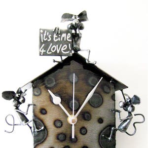 Pode incluir: Um relógio de parede de metal com um design de bolinhas pretas e brancas. Três ratos estão presos ao relógio, um no topo segurando um cartaz que diz "It's time 4 love!" e dois nos lados.