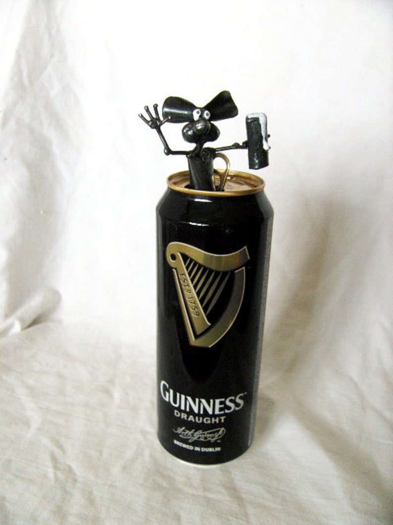 May include: A black metal figurine of a dog holding a can of Guinness Draught beer. The can is black with gold lettering and a harp logo. The text on the can reads "ESTD 1778" and "GUINNESS DRAUGHT".