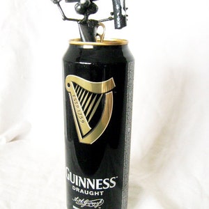 May include: A black and gold Guinness can with a black metal sculpture of a dog holding a bottle opener on top. The can says "Guinness Draught" and "Brewed in Dublin".