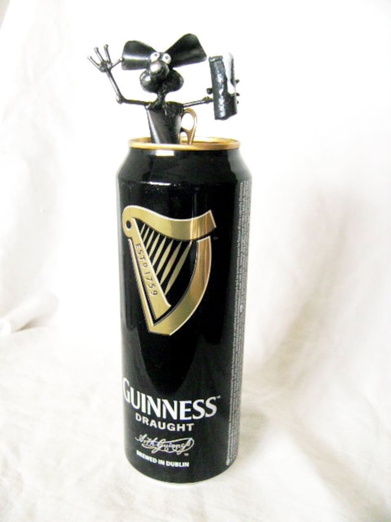 May include: A black and gold Guinness can with a black metal sculpture of a dog holding a bottle opener on top. The can says "Guinness Draught" and "Brewed in Dublin".