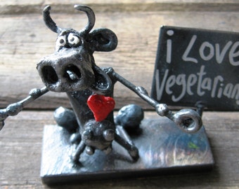 May include: A metal sculpture of a cow holding a red heart and a sign that says "I Love Vegetarians".