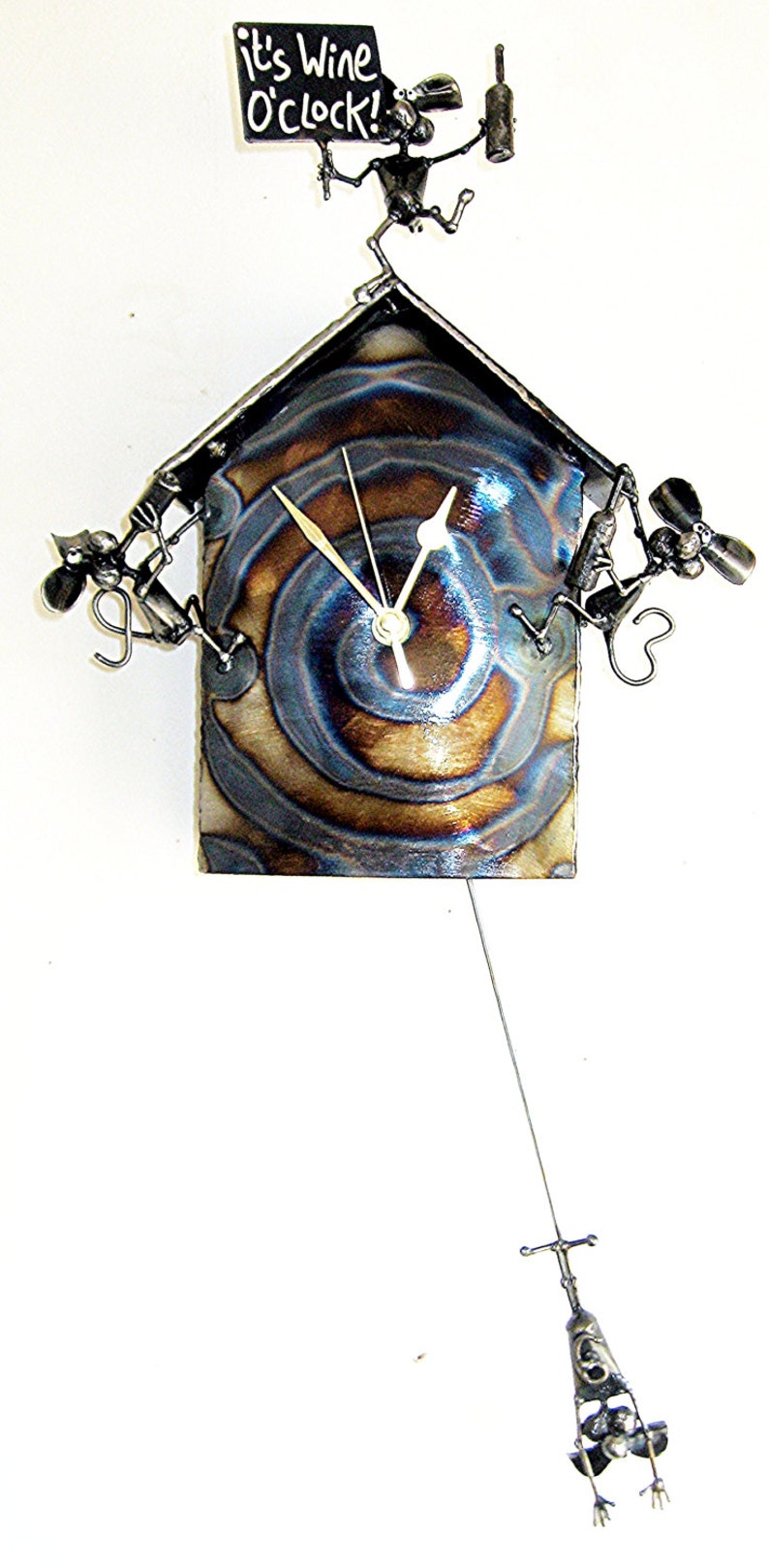 May include: A metal clock with a blue and brown swirl design. The clock is shaped like a house with a metal figure holding a sign that says "It's Wine O'Clock!" and another metal figure holding a bottle of wine. There is a pendulum with a metal figure hanging from the bottom of the clock.