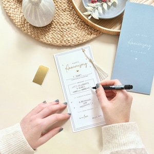 May include: A white card with gold lettering that says "Happy Anniversary 7 Years Together & Counting". The card has a gold tassel and a scratch-off area that says "Scratch to Reveal Your Present". The card also has a message that says "Let's Celebrate 7 Years Happily Married!" and "A Relaxing Spa Weekend!" The card is signed "With Love, Alex XXX".