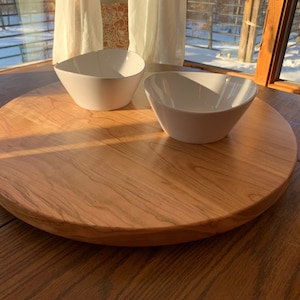 Puede incluir: Una bandeja redonda de servir de madera con un acabado de grano de madera natural. Dos cuencos de cerámica blanca se colocan en la bandeja.