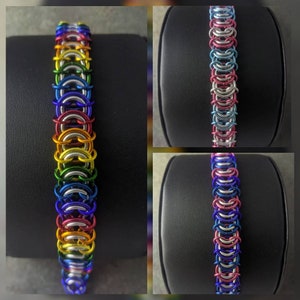 May include: Three bracelets made of metal chain links in different color combinations. The first bracelet is rainbow colored, the second is pink and blue, and the third is blue and purple.
