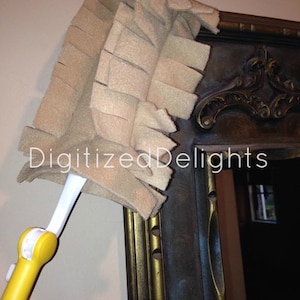 May include: A yellow and white duster with a beige microfiber head is being used to clean a dark brown ornate picture frame.