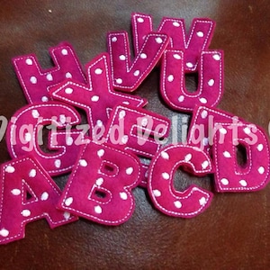 以下が含まれることがあります： 白のドット模様がついた明るいピンク色のフェルト製のアルファベットのセット。アルファベットはA、B、C、D、E、G、H、U、V、Wです。
