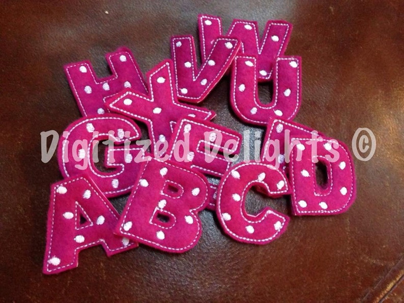May include: A set of felt letters in a bright pink colour with white polka dots. The letters are A, B, C, D, E, G, H, U, V, and W.