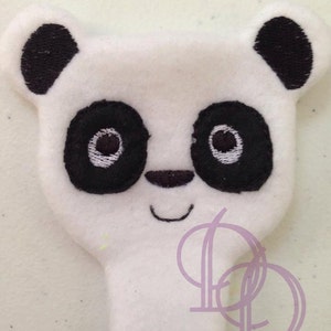 以下が含まれることがあります： 黒く刺繍された目、鼻、耳が付いた白いぬいぐるみパンダの頭。パンダは笑顔の口をしています。