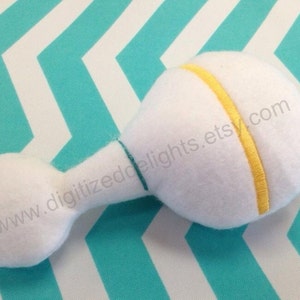 May include: White plush rattle with a yellow stripe and a green seam. The rattle is shaped like a traditional baby rattle.