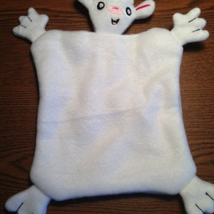 Puede incluir: Manta de seguridad de peluche blanca en forma de cordero con ojos, nariz y boca bordados. El cordero tiene dos brazos pequeños y dos piernas pequeñas.