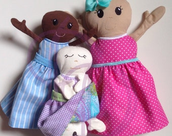 May include: Three handmade fabric dolls. The doll on the left is wearing a blue and white striped dress. The doll in the middle is wearing a purple and white gingham dress with a paisley print. The doll on the right is wearing a pink dress with white polka dots.