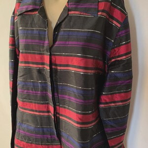 May include: A long-sleeved button-down shirt featuring a black base with horizontal stripes in red, purple, and thin metallic silver. The shirt has a classic collar, a buttoned front placket, and a textured fabric finish throughout the garment.