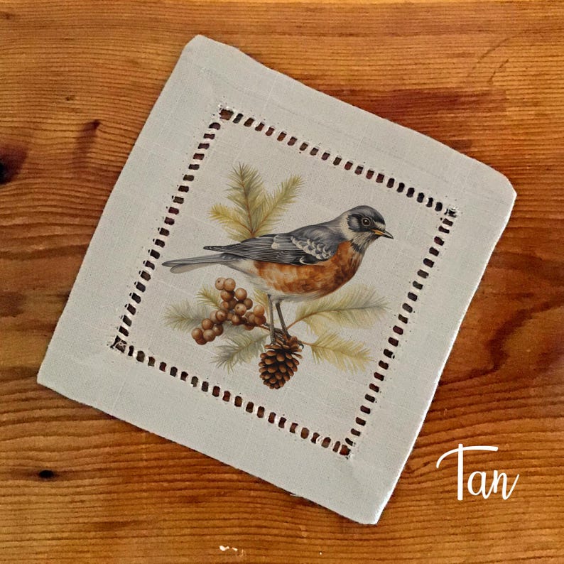 May include: A square, tan-colored coaster with a detailed illustration of a bird perched on a pine cone and branch. The bird has gray, orange, and brown feathers. The coaster has a dotted border and the word "Tan" in the corner.