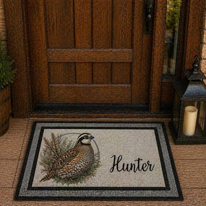 May include: Rectangular doormat with a detailed illustration of a quail and the word "Hunter" in script. The mat has a neutral background with a black border. The quail is brown, white, and black.