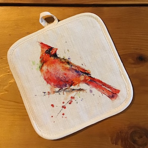 May include: A white cotton pot holder with a red cardinal bird watercolor design. The bird is perched on a branch with red berries.