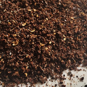 Pode incluir: Close-up de uma mistura de especiarias marrom-escuro com pequenas manchas brancas e marrom-claro. A mistura de especiarias é uma mistura de café moído, sal e pimenta.