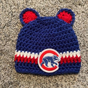 May include: Blue crocheted baby hat with red and white stripes and a Chicago Cubs logo patch.