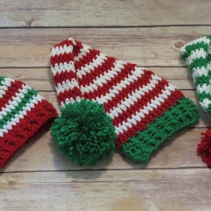 May include: Three crocheted elf hats with white, red, and green stripes. Each hat has a pom-pom on the top.
