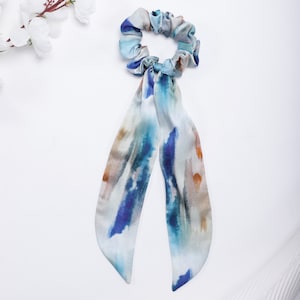 May include: A white, blue, and brown patterned hair scrunchie with long, flowing tails. The scrunchie is made of a soft, silky fabric.