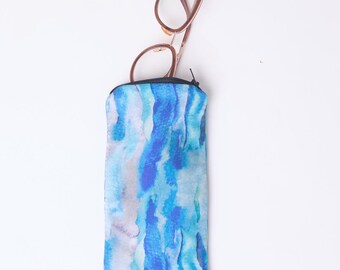 Op de afbeelding: Een rechthoekige brillenkoker met een blauw en wit aquarelpatroon, met een bril met bruin montuur. De koker heeft een zwarte ritssluiting en heeft een abstract patroon.