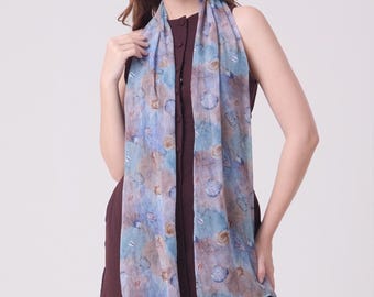 May include: A light blue and brown scarf with a seashell pattern. The scarf is draped over a dark burgundy dress. The scarf has a watercolor effect with shades of blue, brown, and white. The scarf is made of a lightweight fabric.