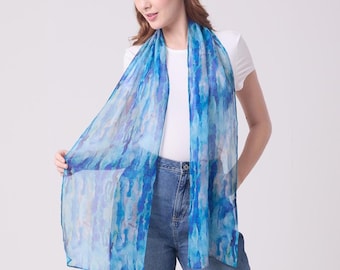 May include: A sheer, lightweight scarf with a watercolor-style design in shades of blue. The scarf is draped around the neck and shoulders, creating a flowing, elegant look. The fabric appears to be delicate and semi-transparent, with a subtle sheen.