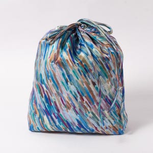 Könnte beinhalten: Eine Kordeltasche aus blauem Satin mit einem bunten abstrakten Muster aus blauen, grünen, braunen und violetten Pinselstrichen.